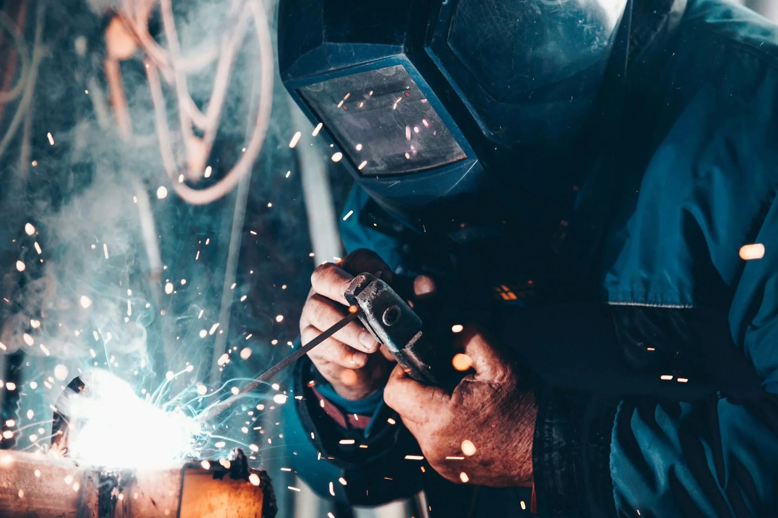 A person welding metal with sparks flying, wearing protective gear including a welding helmet and gloves.