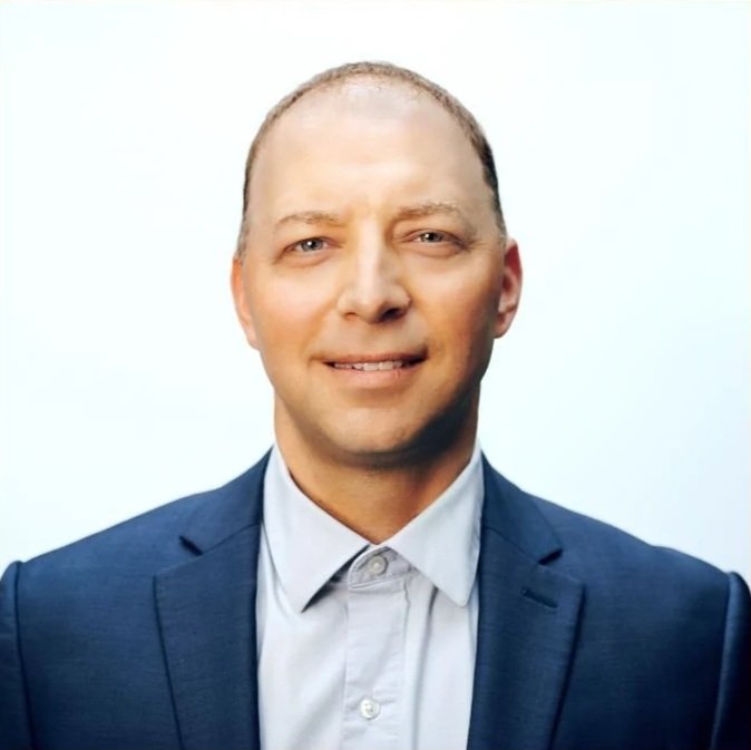 A man in a blue suit smiling at the camera, with a light background.