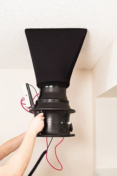 A person holds a black loudspeaker mounted on a wall.