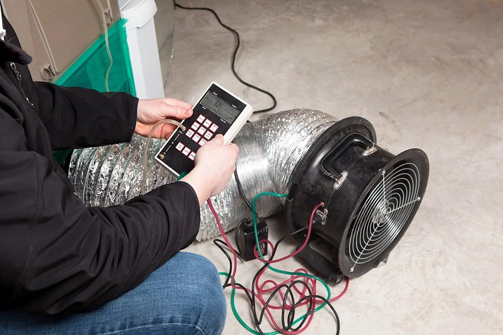 Person checking a HVAC or air ventilation system using a digital device with wires connected to a large duct fan.