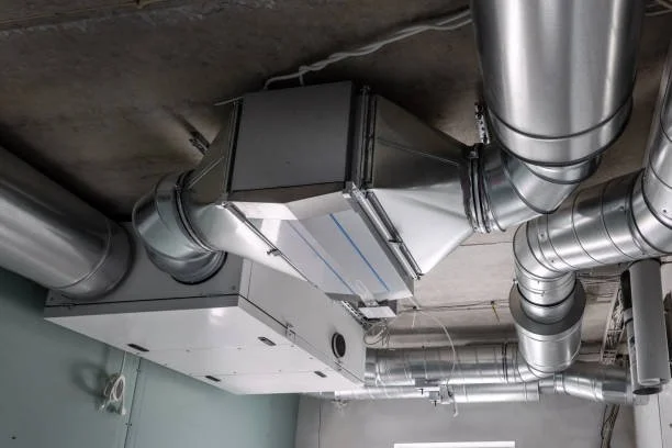 Ceiling-mounted HVAC ventilation system with metallic ducts and an air handling unit in a commercial or industrial building.