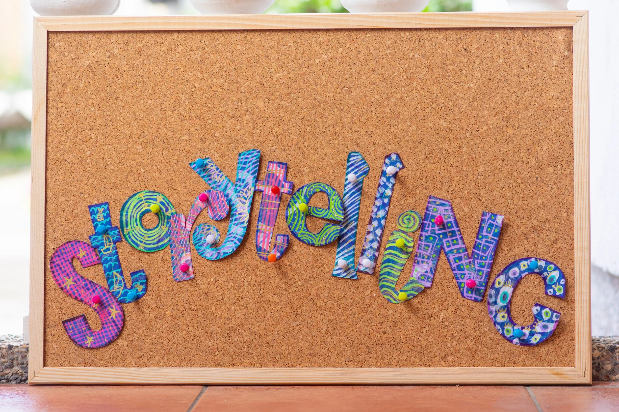 Colorful decorative letters spelling 'SCHOOLING' pinned on a cork bulletin board.