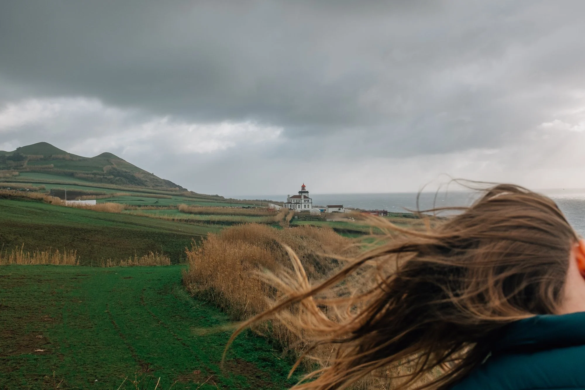 Kendal catching wind at Miradouro da Ilha Sabrina. Farol da Ferraria lighthouse in background.