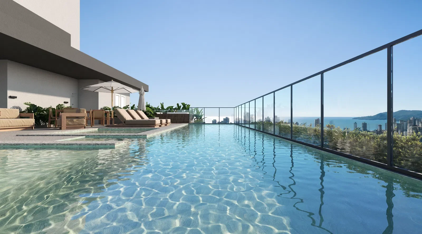 Piscina de terraços em um prédio alto com vista para a cidade e o mar, cadeiras e guarda-sóis ao redor, sob céu claro.