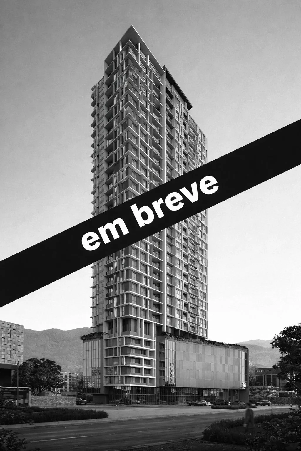 Prédio alto de arquitetura moderna com muitas janelas, sob céu claro, em área urbana com montanhas ao fundo, em preto e branco. Texto 'em breve' em faixa diagonal.