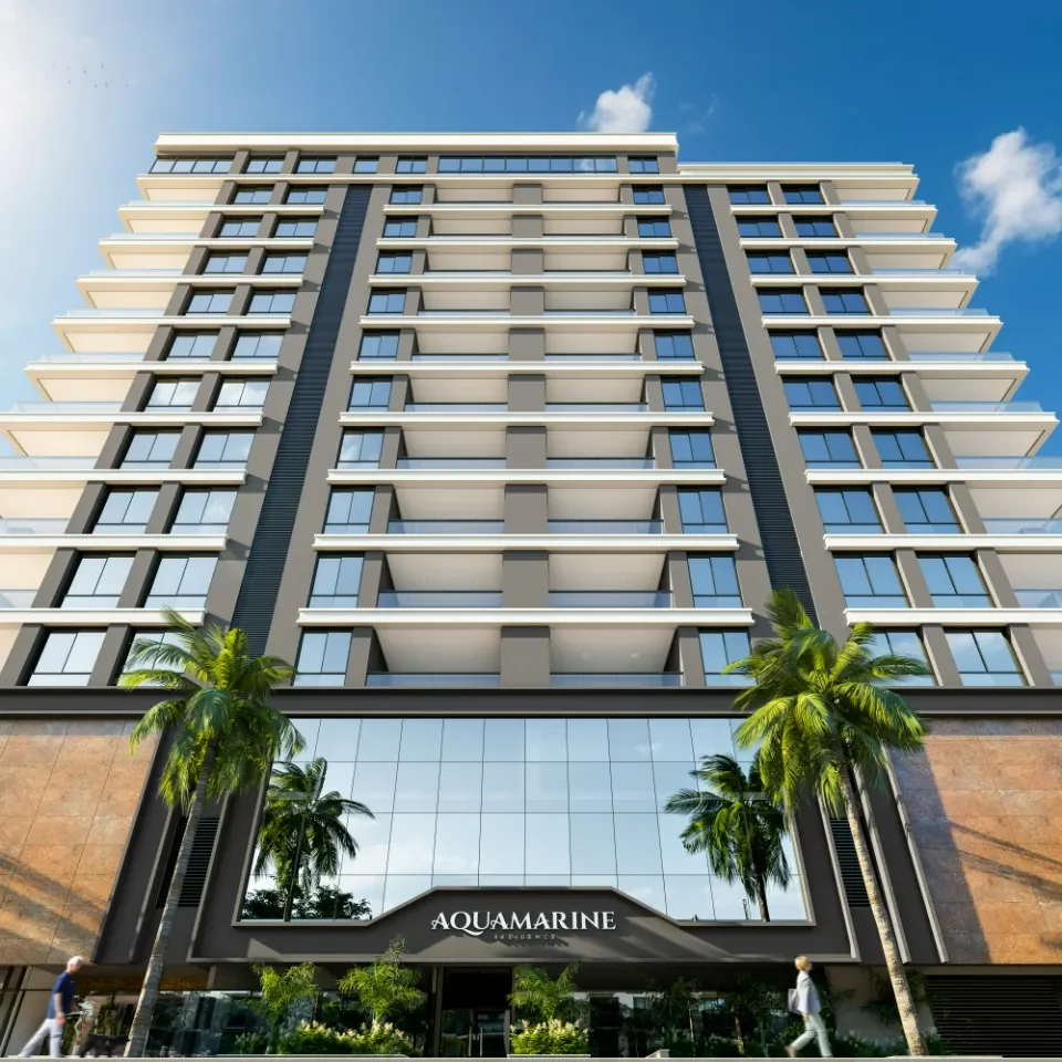Imagem de um prédio moderno de vários andares com fachada de vidro, em frente há palmeiras e duas pessoas caminhando, sob céu azul com algumas nuvens e o nome 'Aquamarine' na entrada.