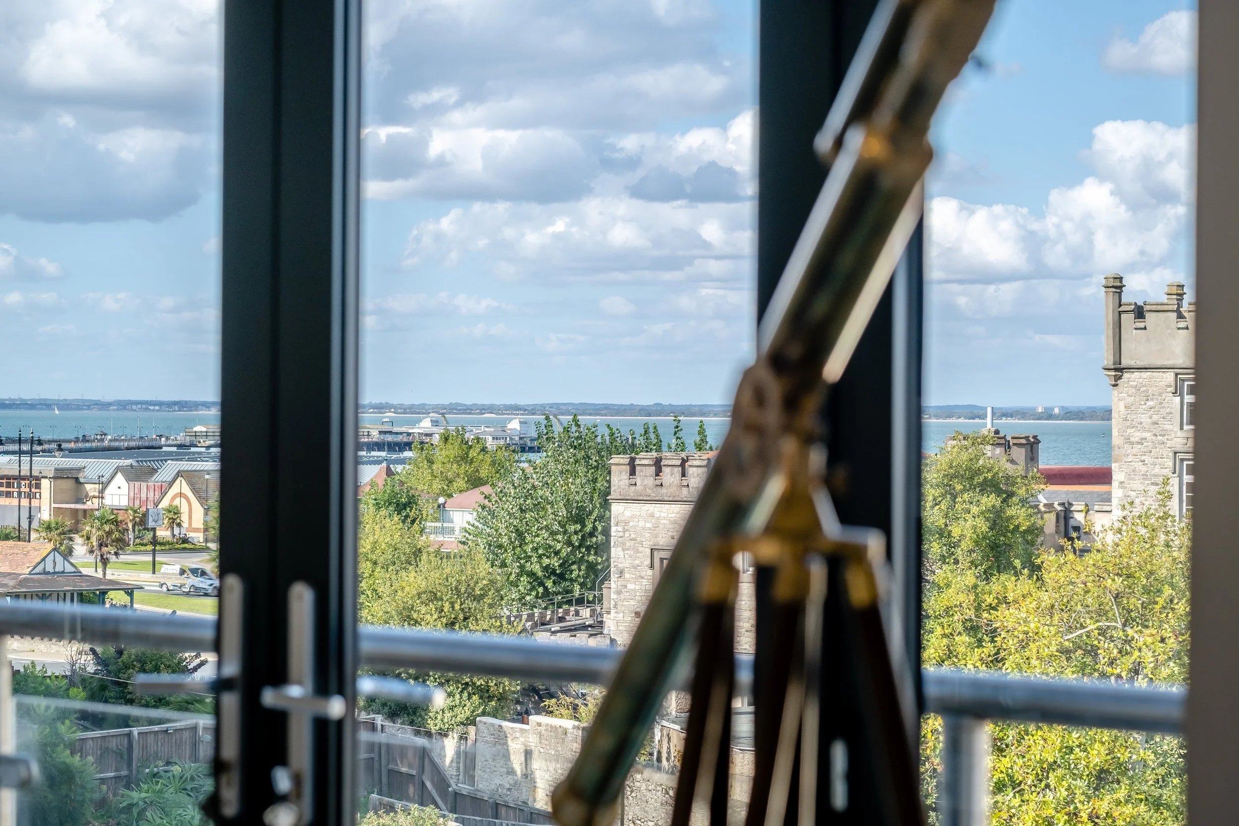 View through a large window of a harbor with boats, a cloudy sky, and buildings, with a wooden easel partially visible inside the room.