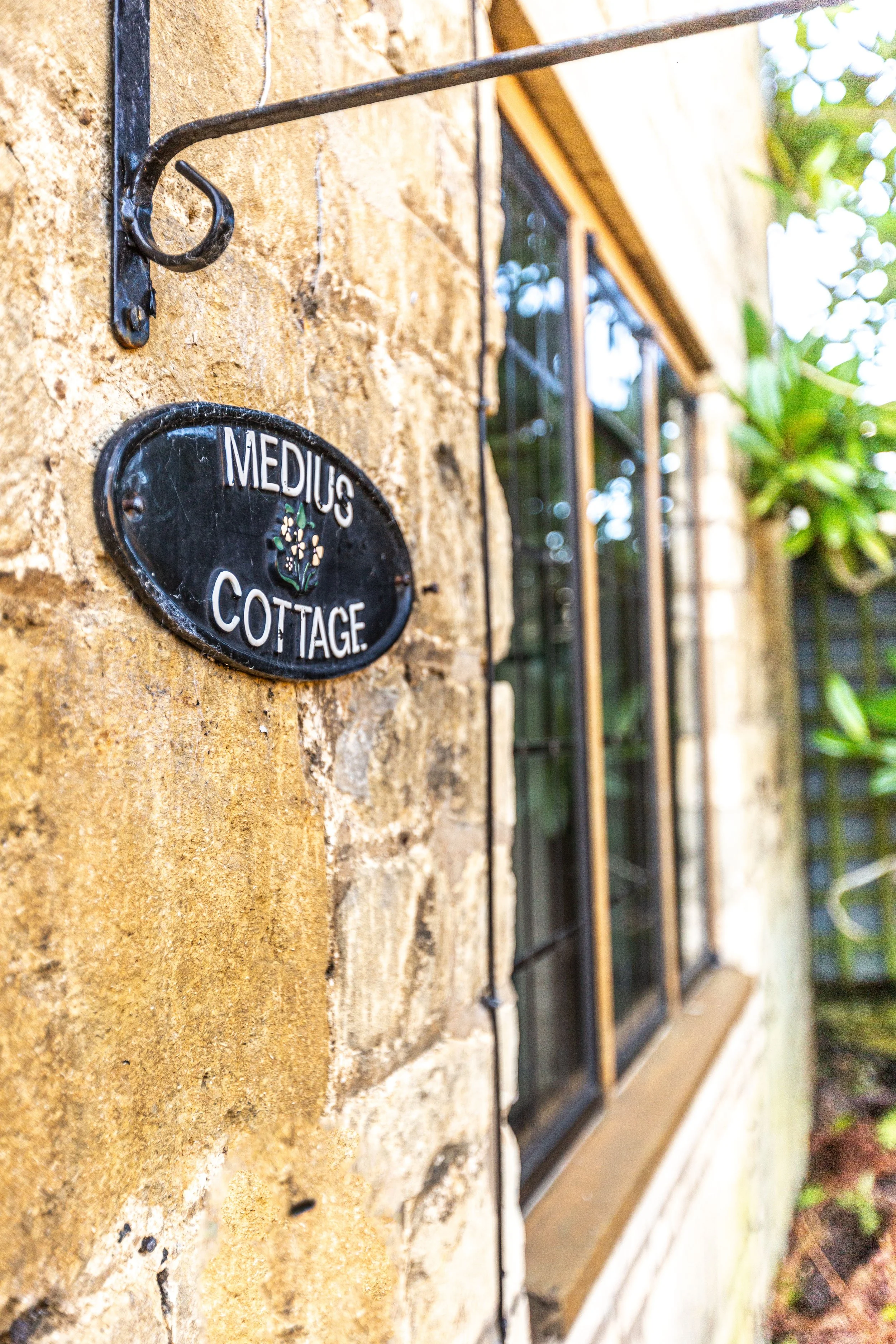 Close-up of a black oval sign on a brick wall that reads 'Medicus Cottage' with a small floral design in the center.