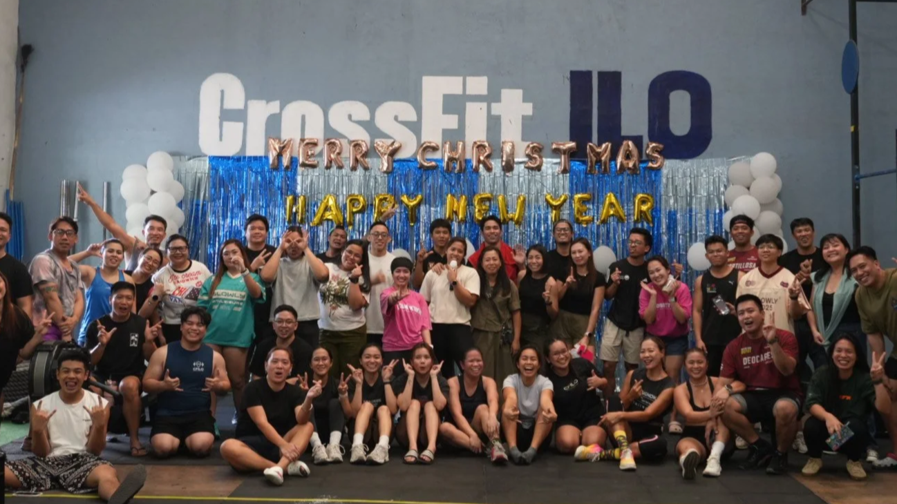 Group of people posing together at a CrossFit gym during a Christmas and New Year celebration, with festive decorations and banners.