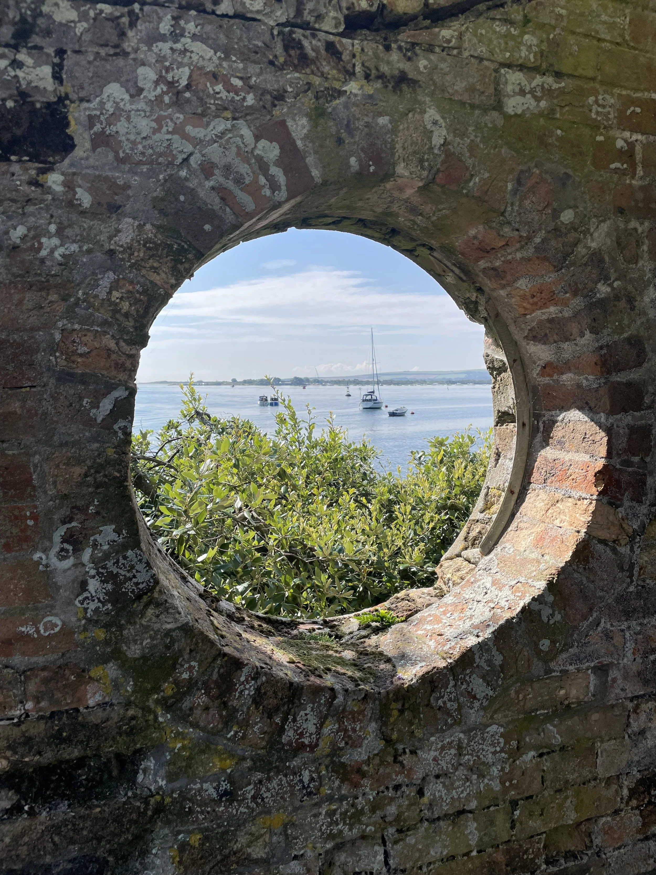 View through a circular stone opening towards water and boats.