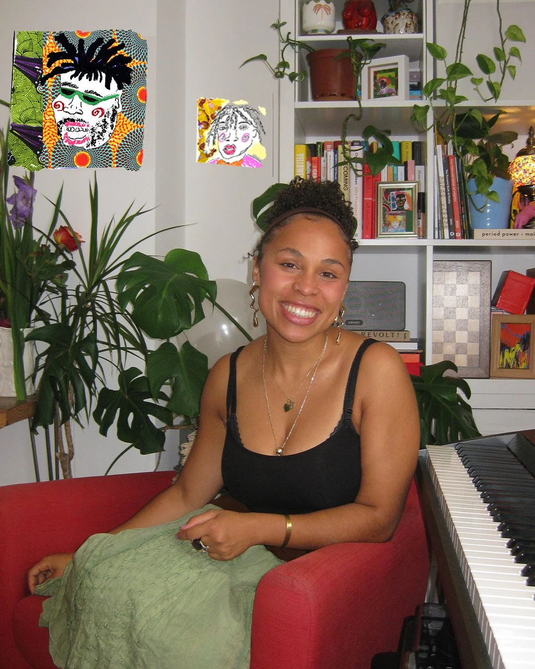 A woman with curly hair in a bun, wearing a black tank top and green skirt, smiling and sitting on a red chair in a room with plants, books, and artwork on the wall beside a keyboard.