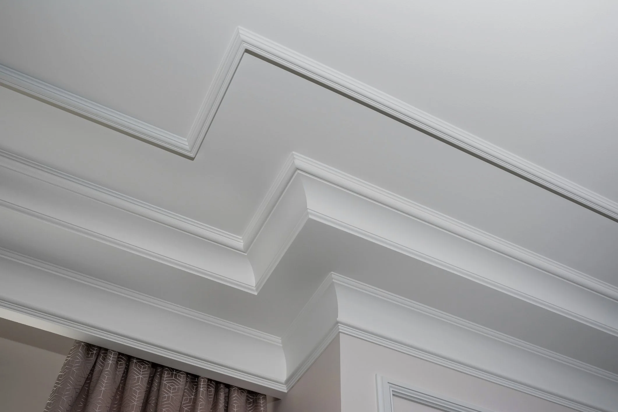 Ceiling with decorative crown molding and a section of patterned curtains.