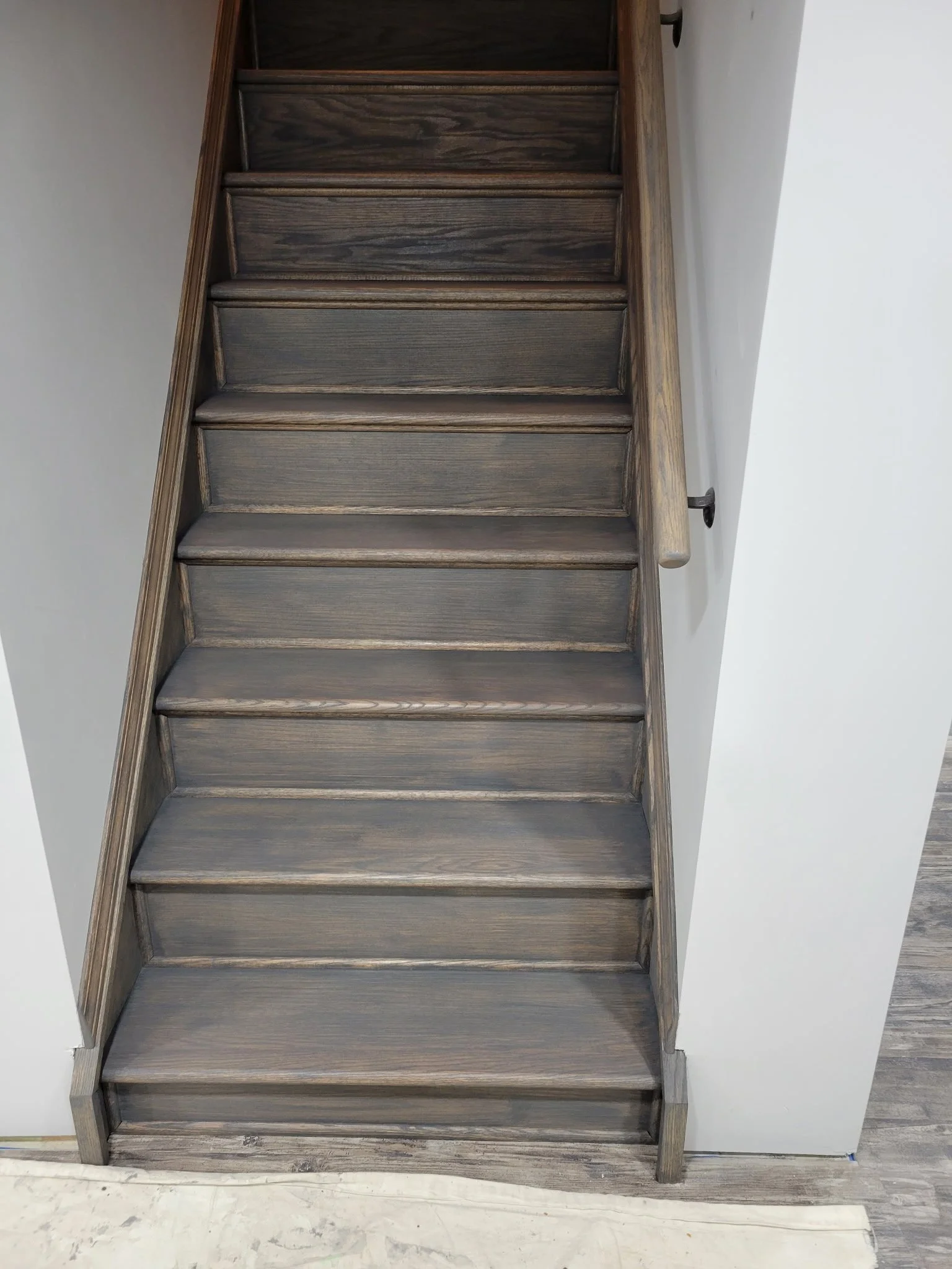Top view of a wooden staircase with nine steps, dark wood finish, and a light-colored wall on the side.