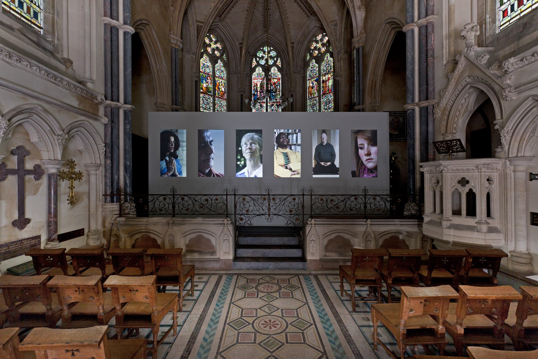A digital art installation with seven large vertical screens displaying black-and-white portraits of different people's faces inside a dark room.