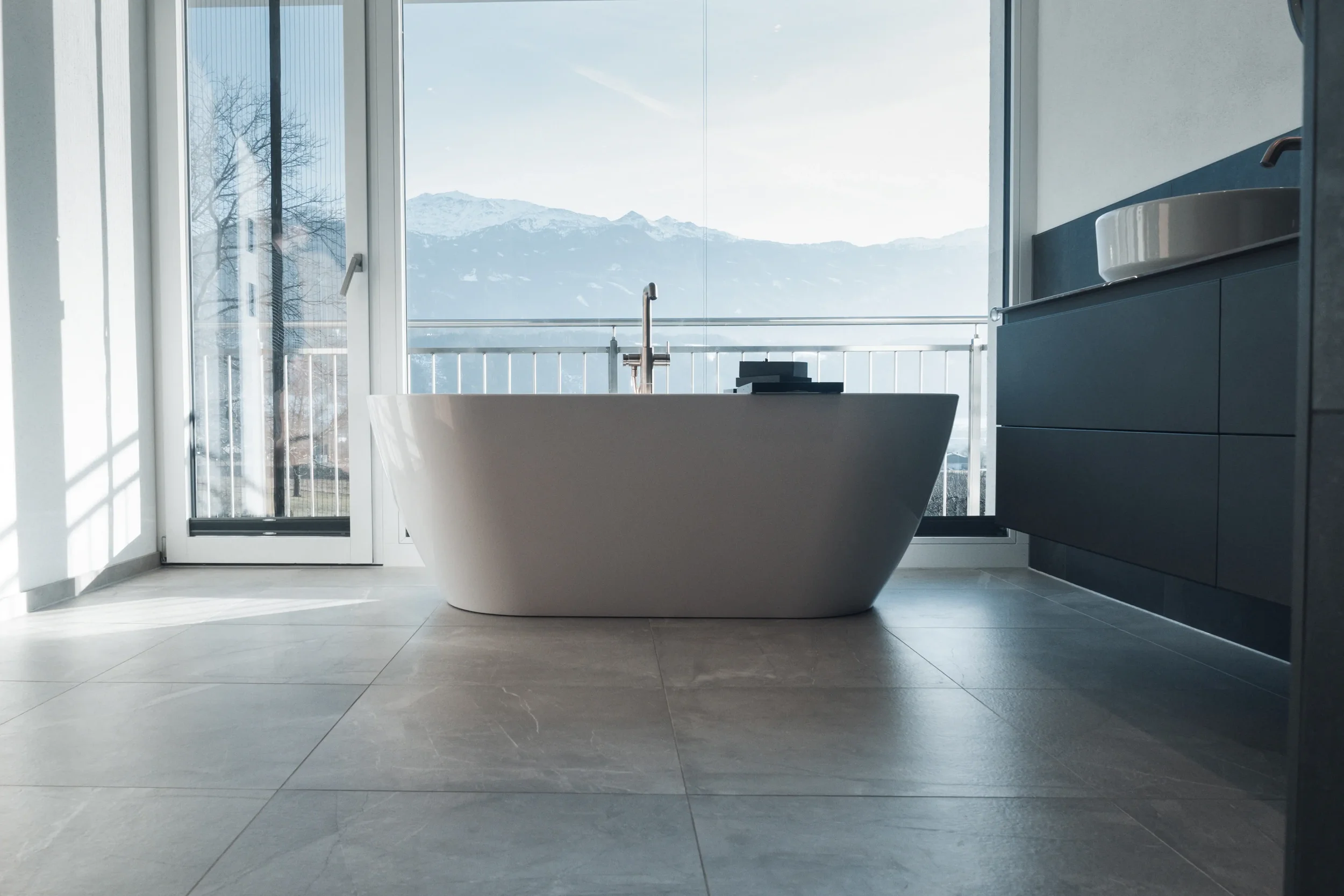 Modernes Badezimmer mit freistehender Badewanne vor einem großen Fenster mit Bergblick.