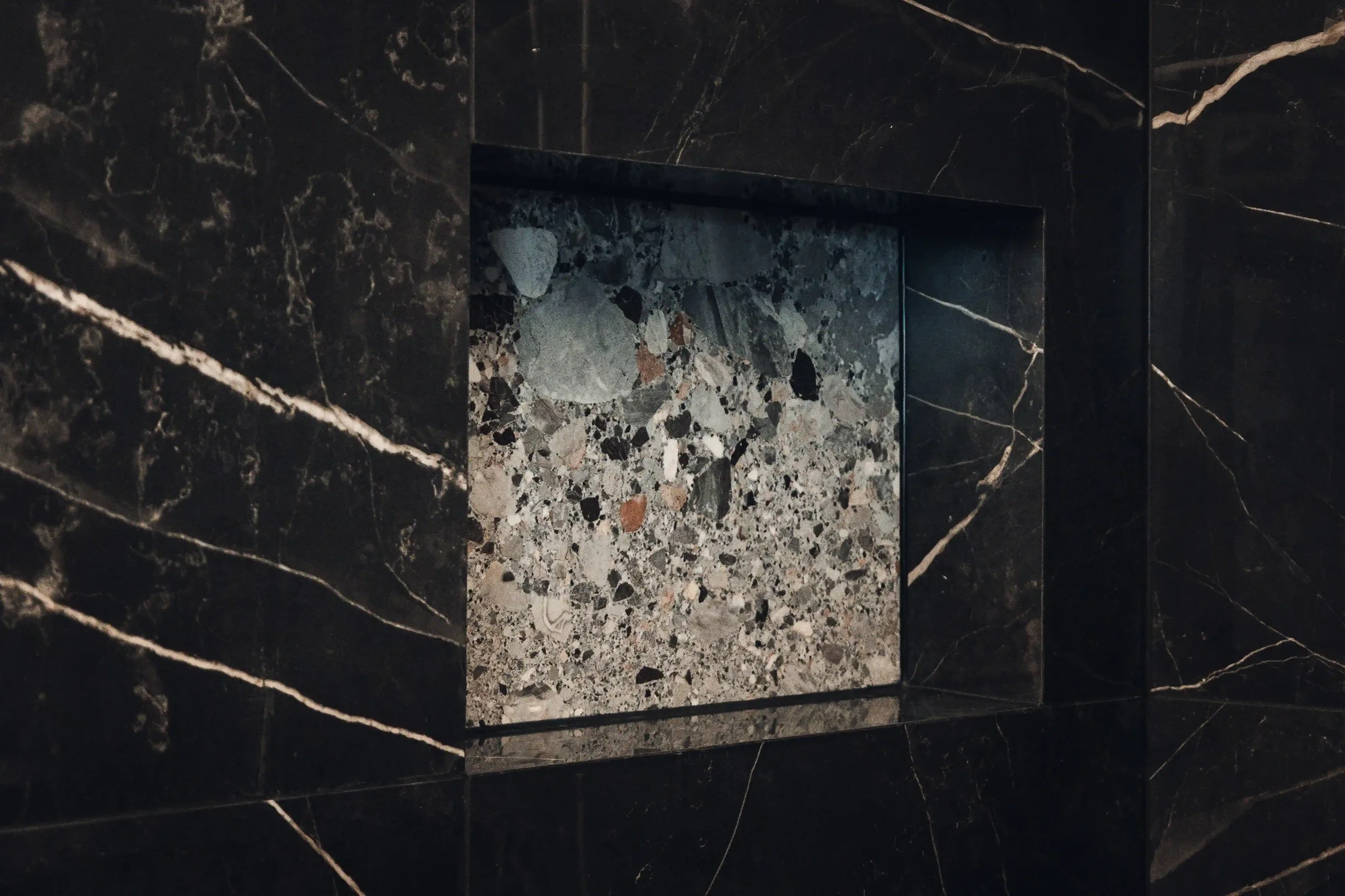 Ein Kamin mit dunklem, schwarzen Marmorrahmen und einer eingebauten Feuerstelle mit einer Oberfläche aus Mosaiksteinchen in Grau, Schwarz und Braun.