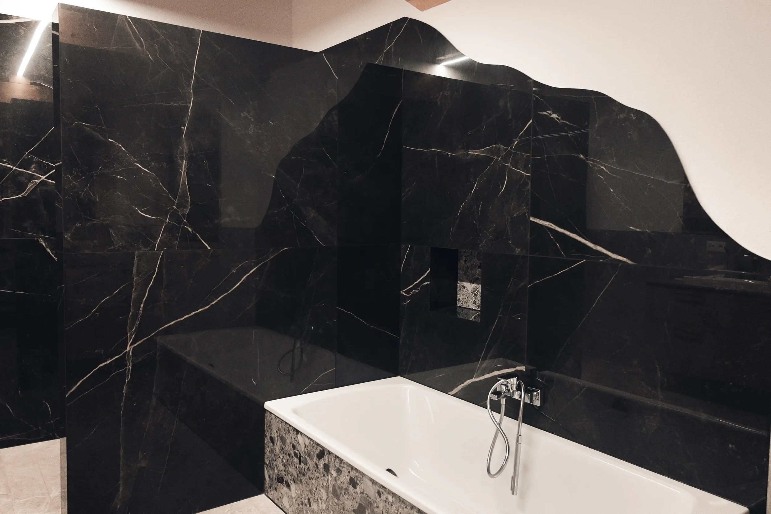 Moderner Badezimmer mit schwarzer Marmorwand, Badewanne und Handbrause, spiegelreflexartige Oberfläche