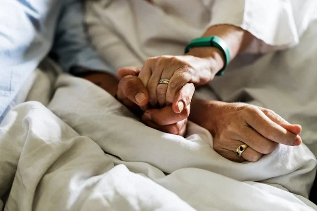 hospice patient holding hands in bed