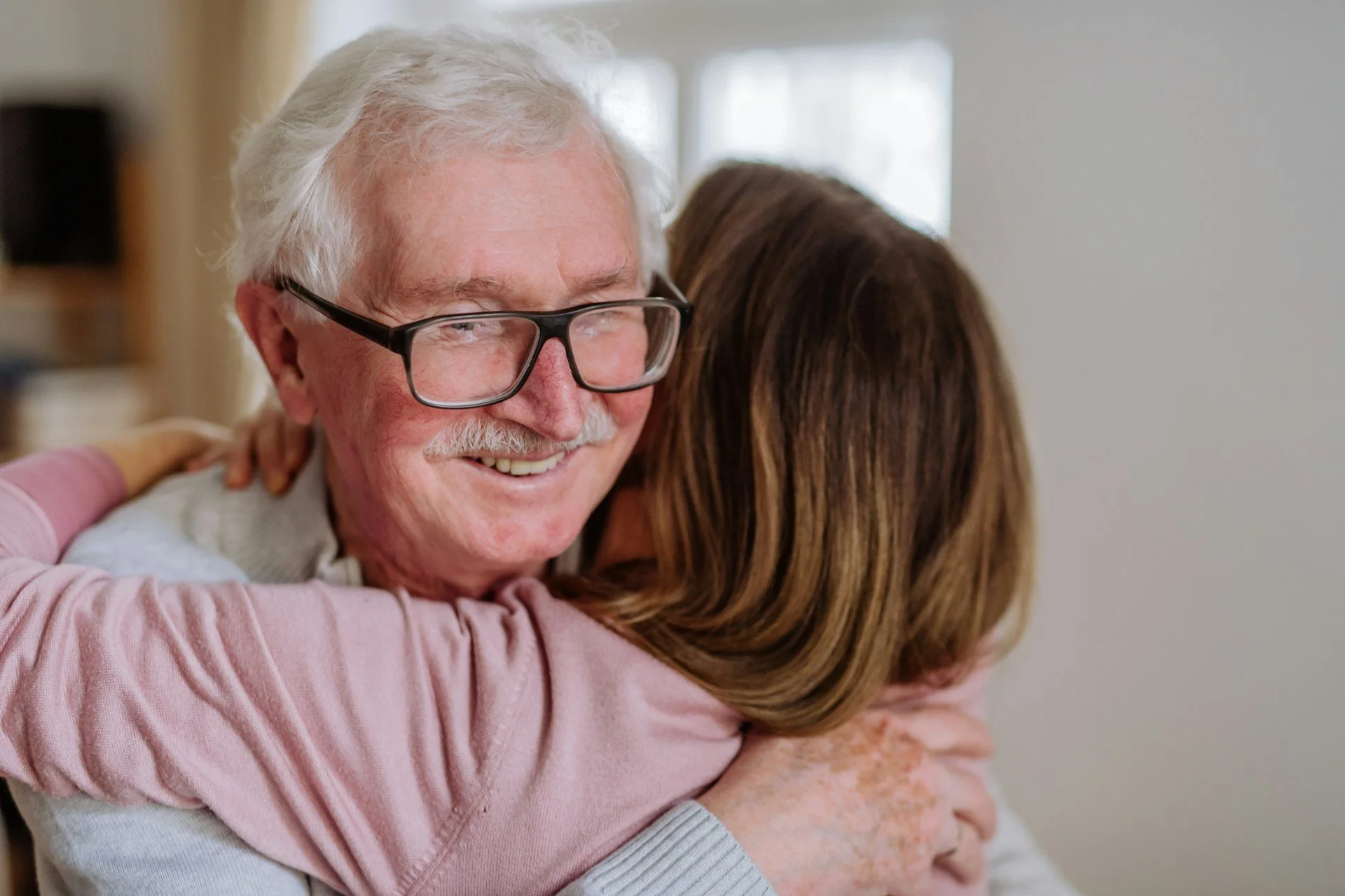 older man smiling and receiving a hug from caregiver