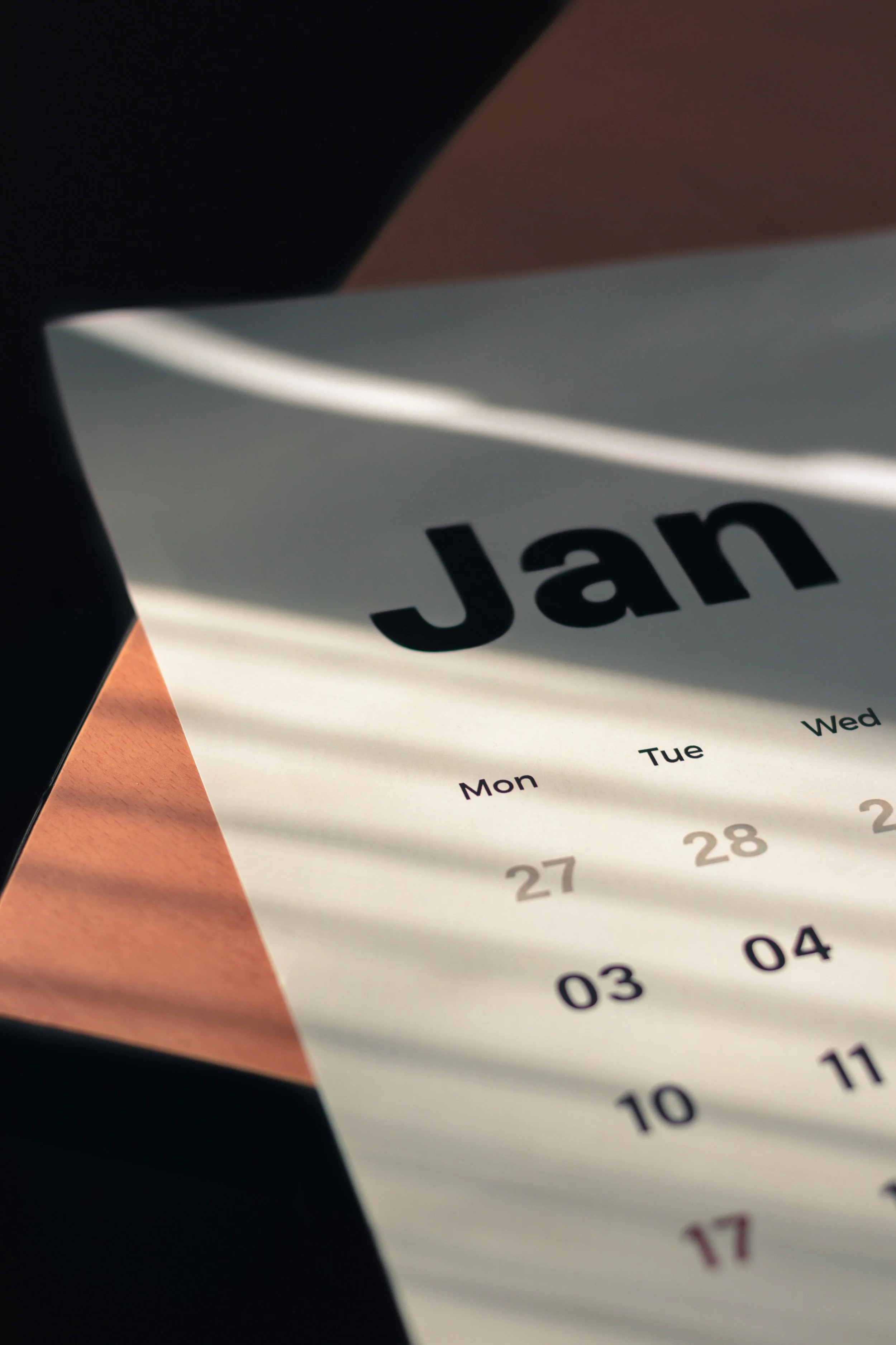 Close-up of a paper calendar showing the month of January with the dates from 27 to 30, with sunlight creating shadow lines across it.