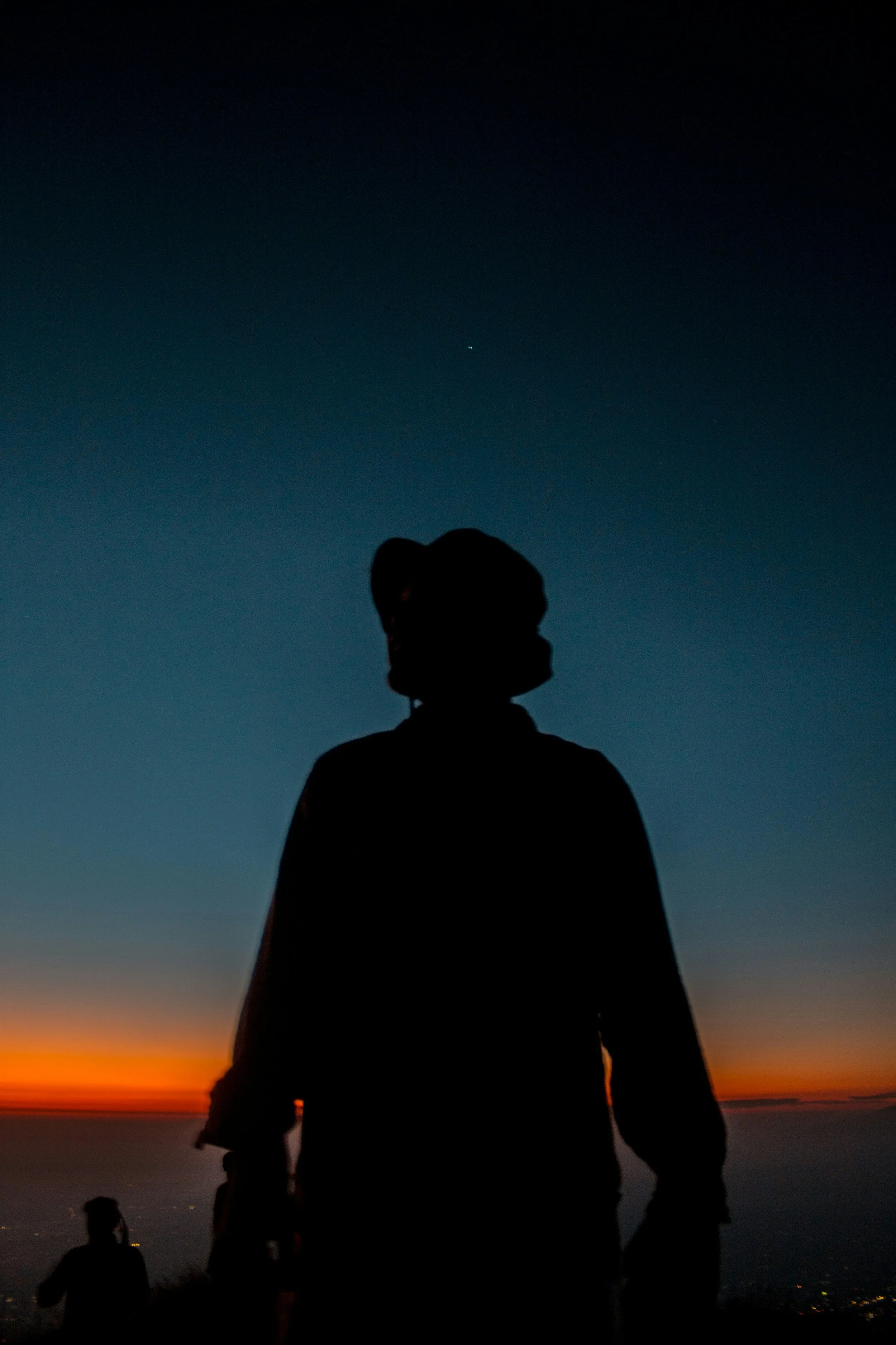 Silhouette of person outdoors during sunset with a clear darkening sky and distant city lights.