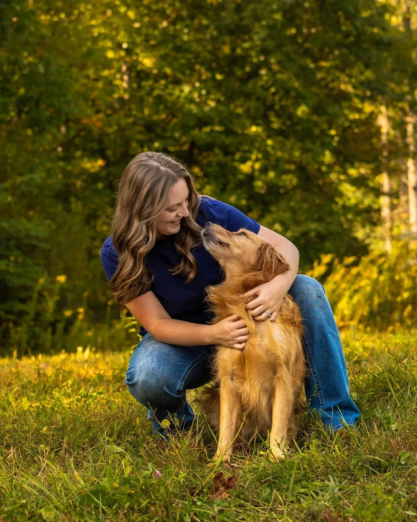A woman hugging a golden retriever dog in a grassy field during autumn.