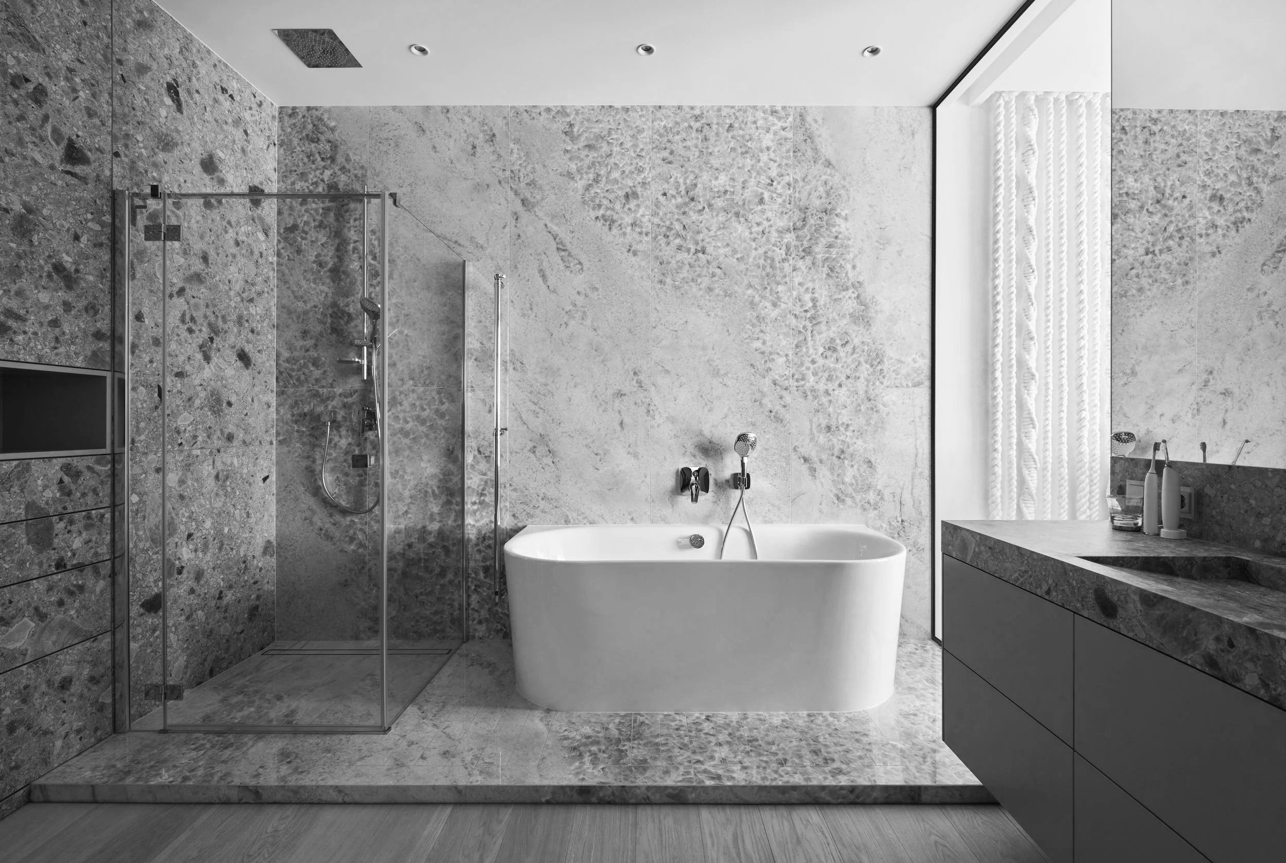 Modern bathroom with a freestanding bathtub, a glass-enclosed shower, and a marble vanity with toiletries, all in grayscale.