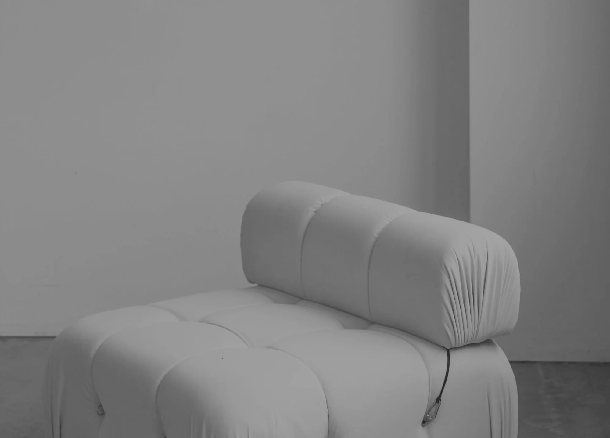 A white cushioned chair with a headrest, positioned against a plain wall, in a minimalistic room.