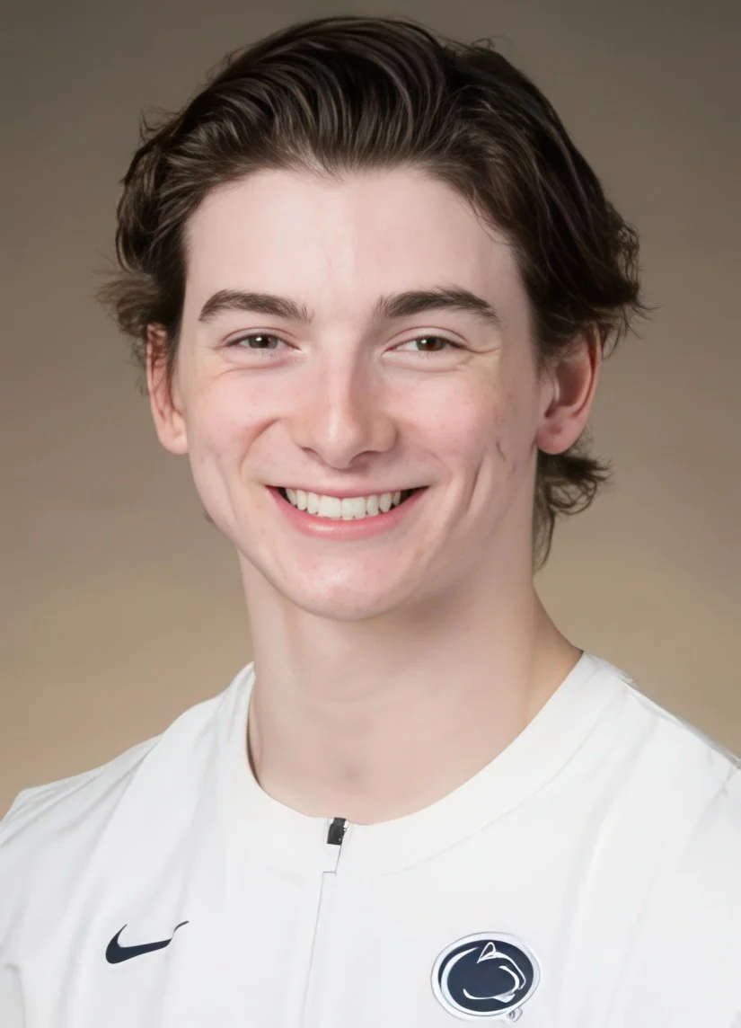 A young man with brown hair smiling, wearing a white sports jersey with a Nike logo and a Penn State logo on the chest.