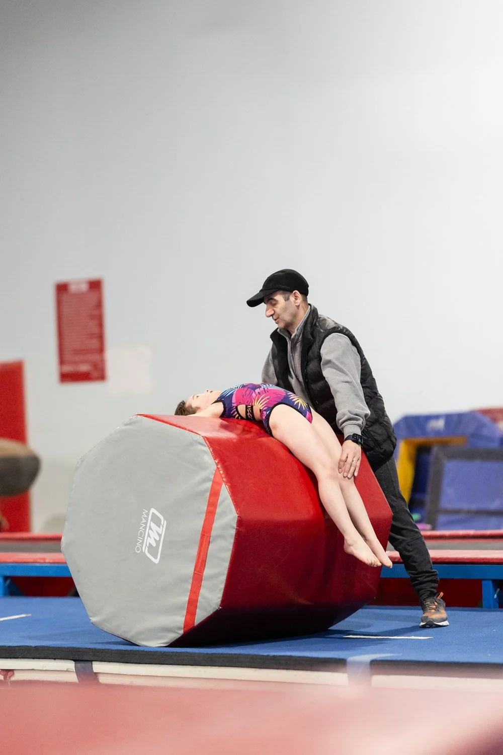 A gymnast practicing on a tumbling roller with a coach in a gymnastics facility.