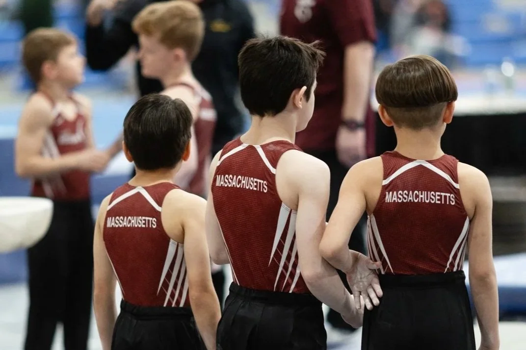 Young boys in red and white sports uniforms with 'Massachusetts' printed on the back, standing in a gymnasium before a gymnastics activity.