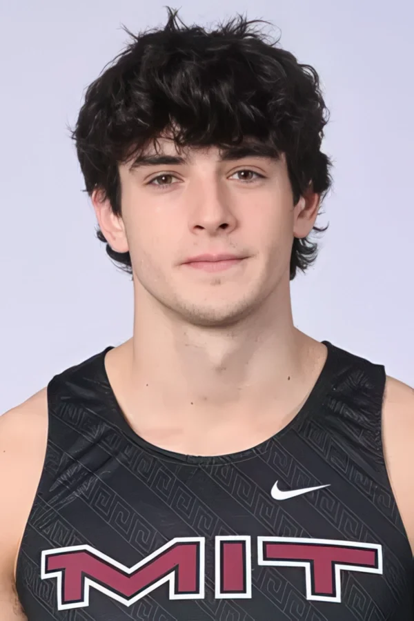 A young man with dark, curly hair and light skin wearing a black athletic jersey with a Nike logo and the word "MUT" printed on it, smiling slightly.