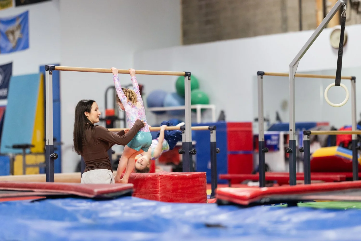 A woman spotting a young girl doing gymnastics on a balance beam in a gymnasium.