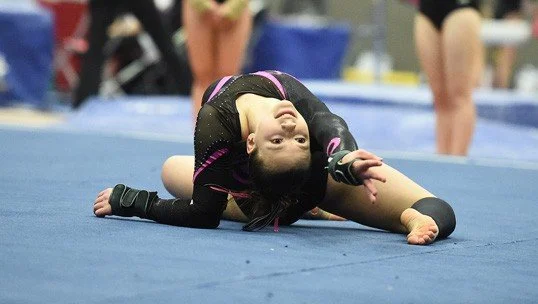 Young girl in a gymnastics uniform stretching on the mat during a gymnastics event.