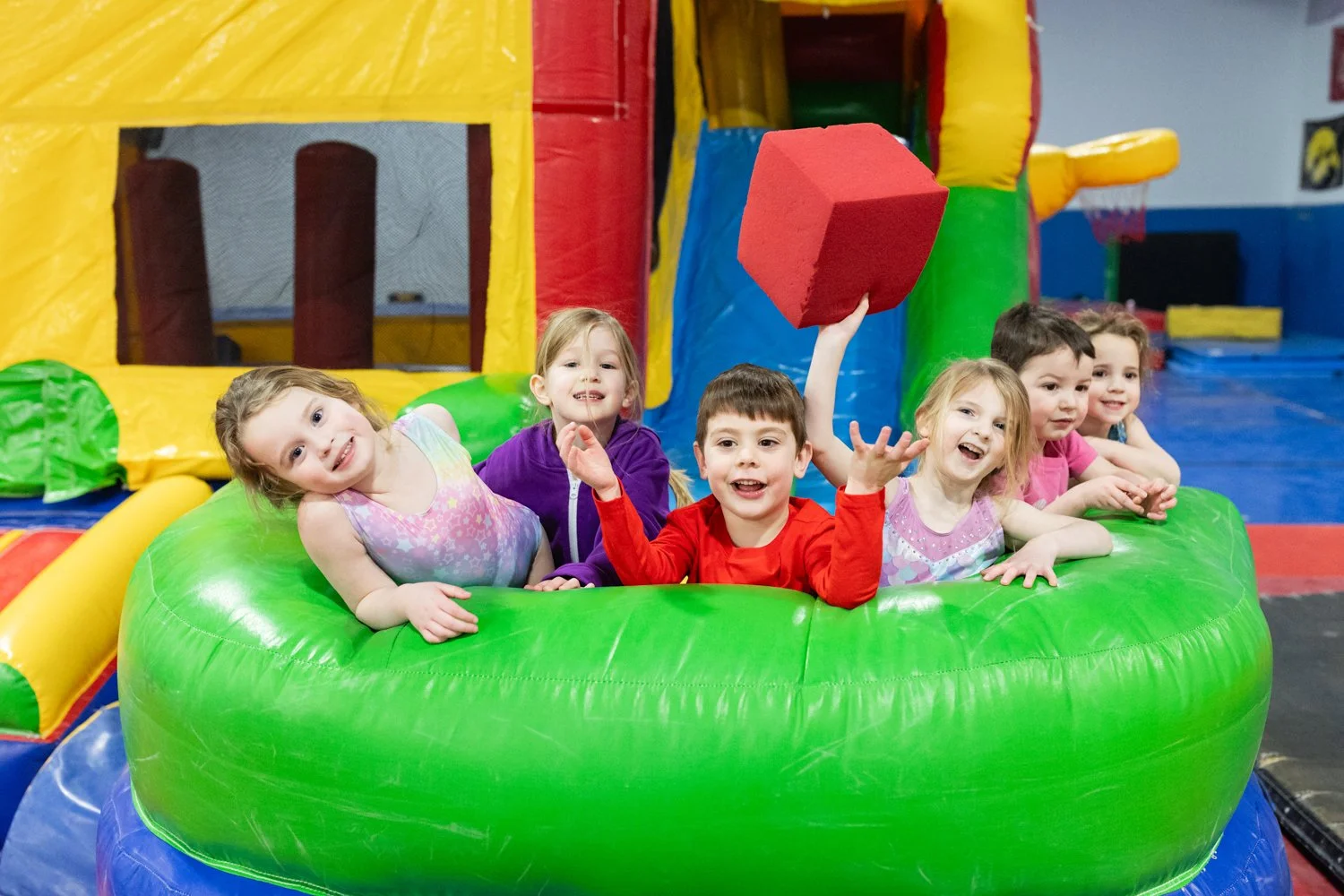 Group of young children smiling and playing in an inflatable bounce house with colorful walls at an indoor playground.
