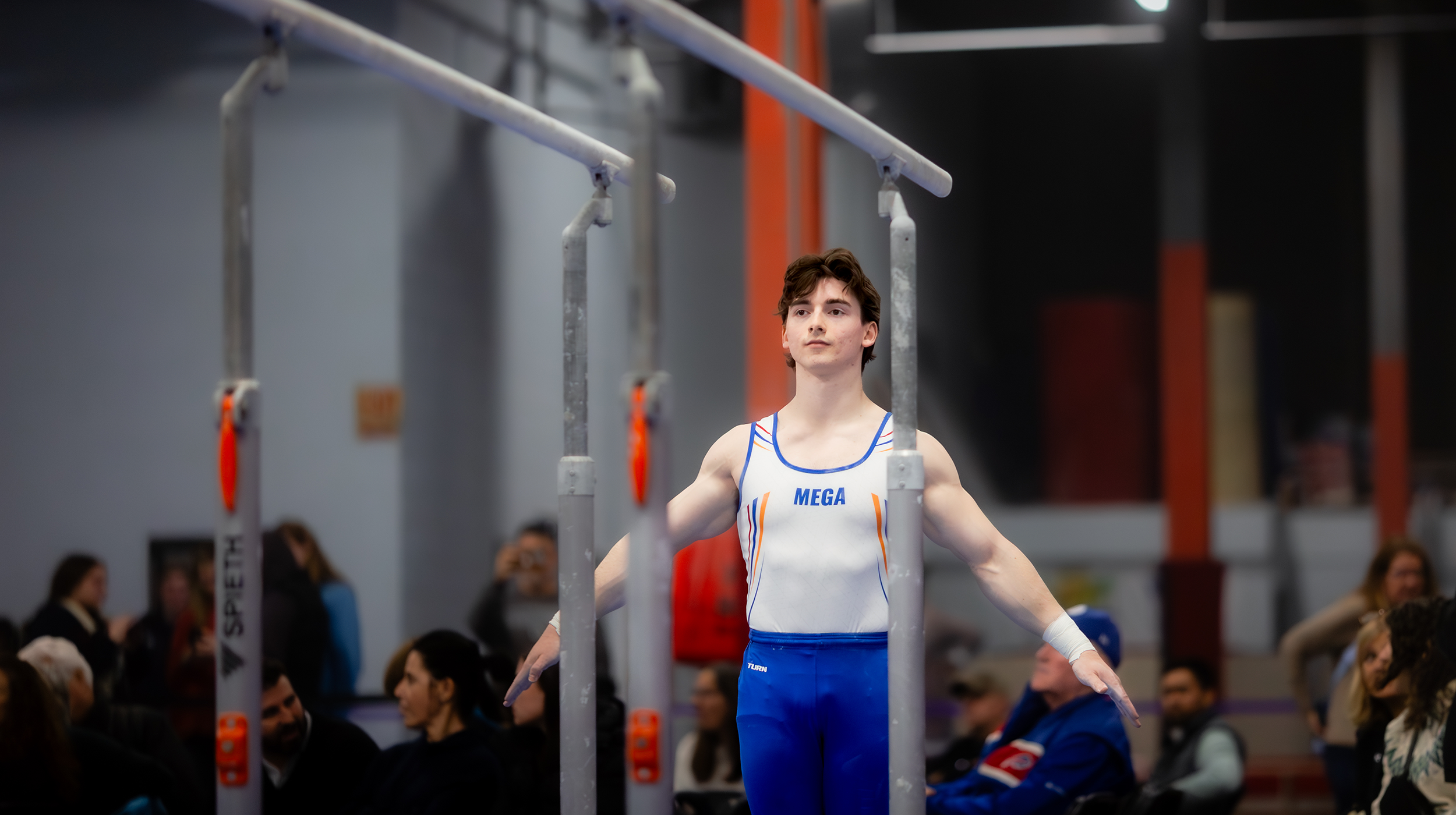 A male gymnast performing a handstand on parallel bars during competition.