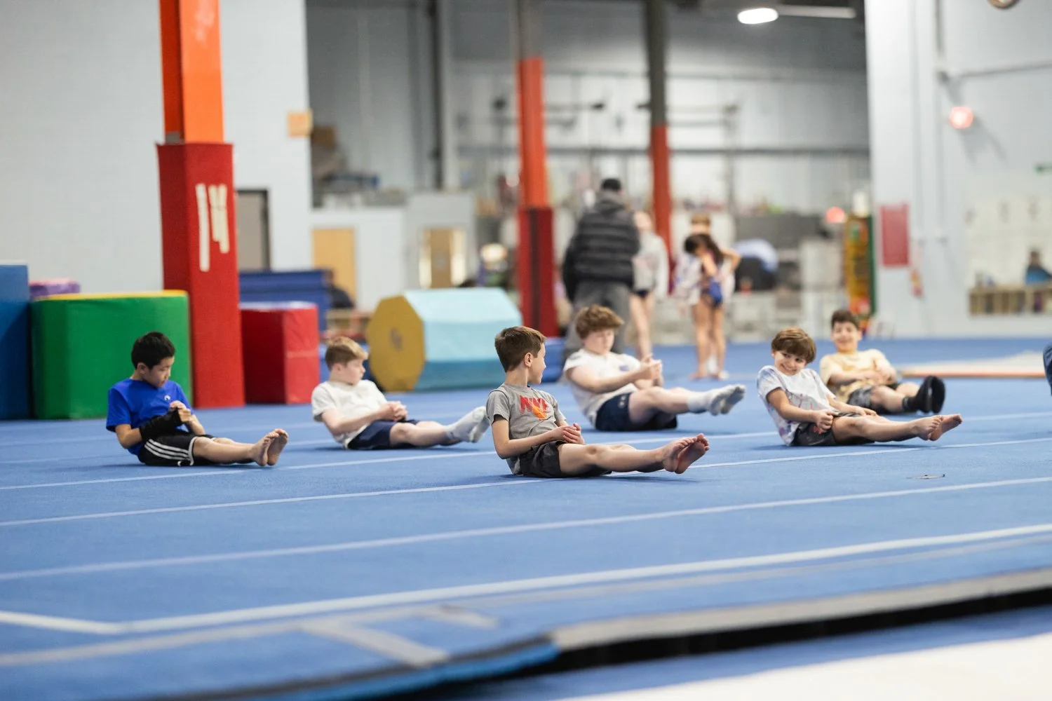 Children sitting on the floor of an indoor gym, stretching or warming up before exercise.