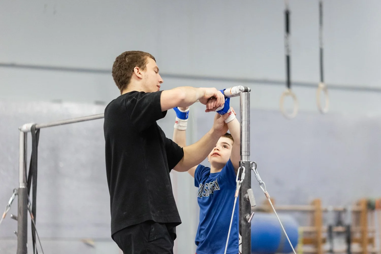 A young man helping a boy with gymnastics equipment in a gymnasium.