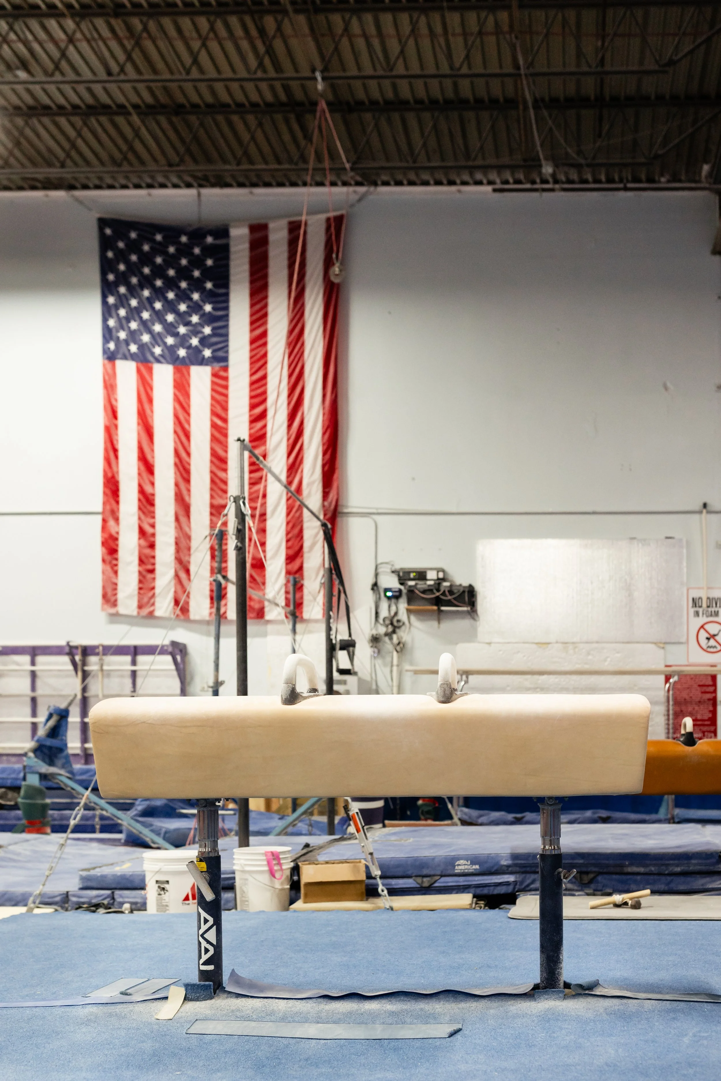 Gymnastics gym with uneven bars and American flag hanging on the wall.
