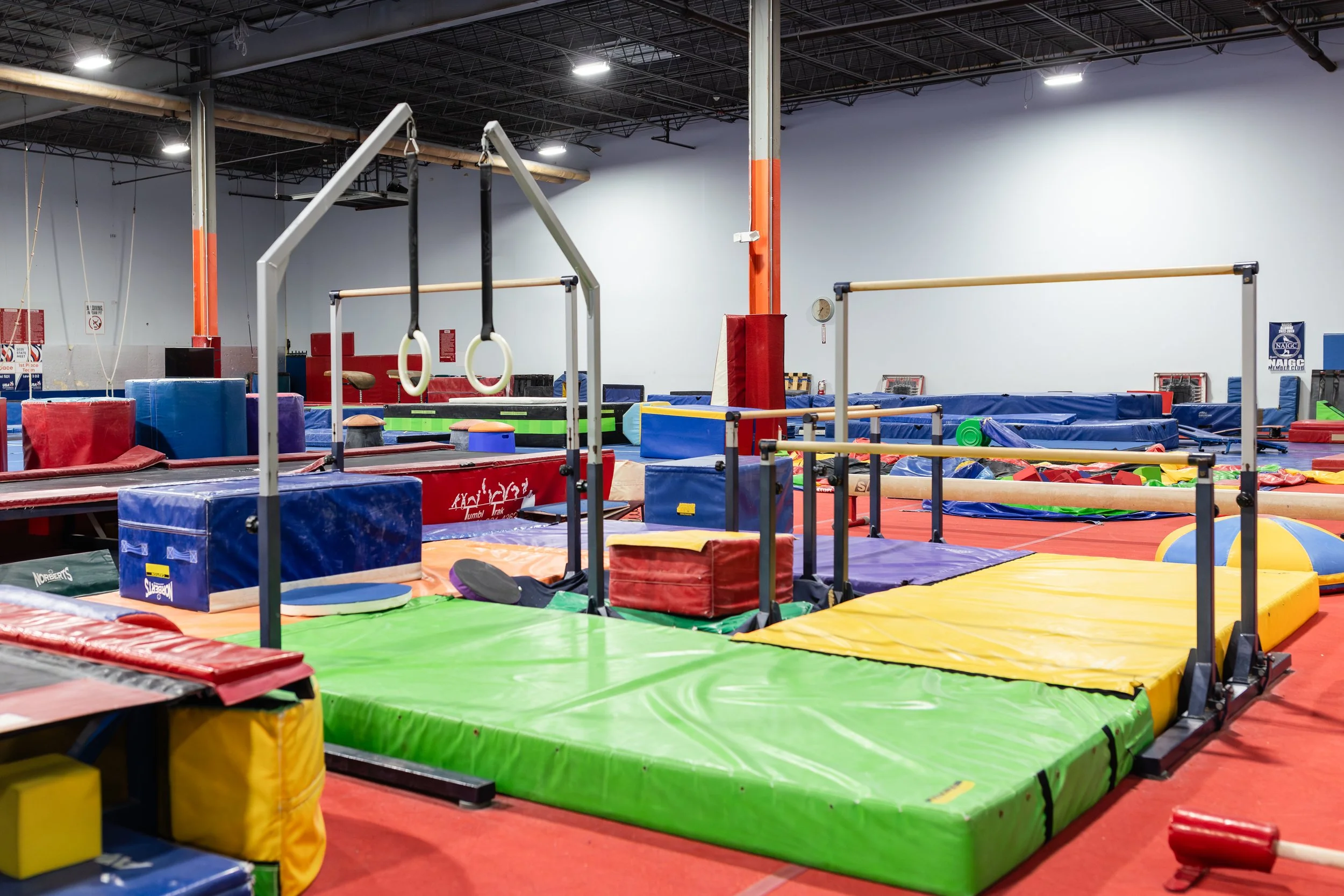 Indoor gym with foam mats, gymnastics equipment, and padded surfaces for children's activities.