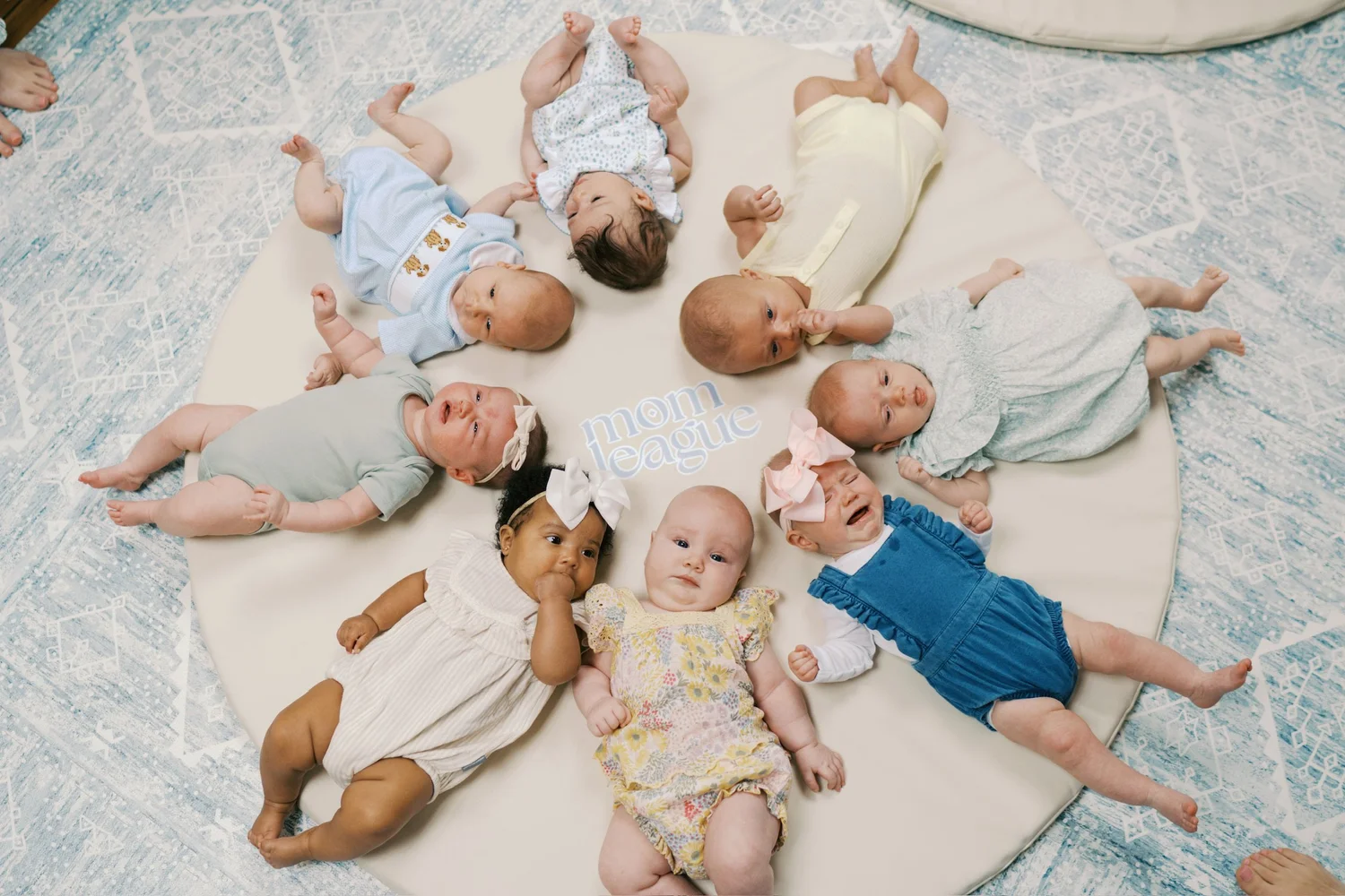 Eight babies lying in a circle on a round play mat