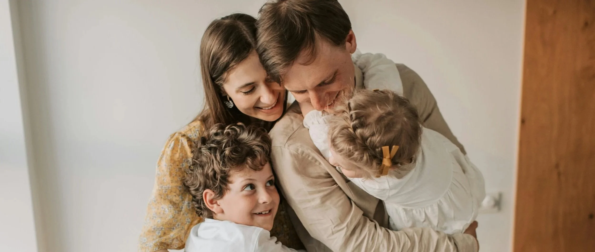 La mère, le père et leurs deux jeunes enfants s'enlacent et sourient.