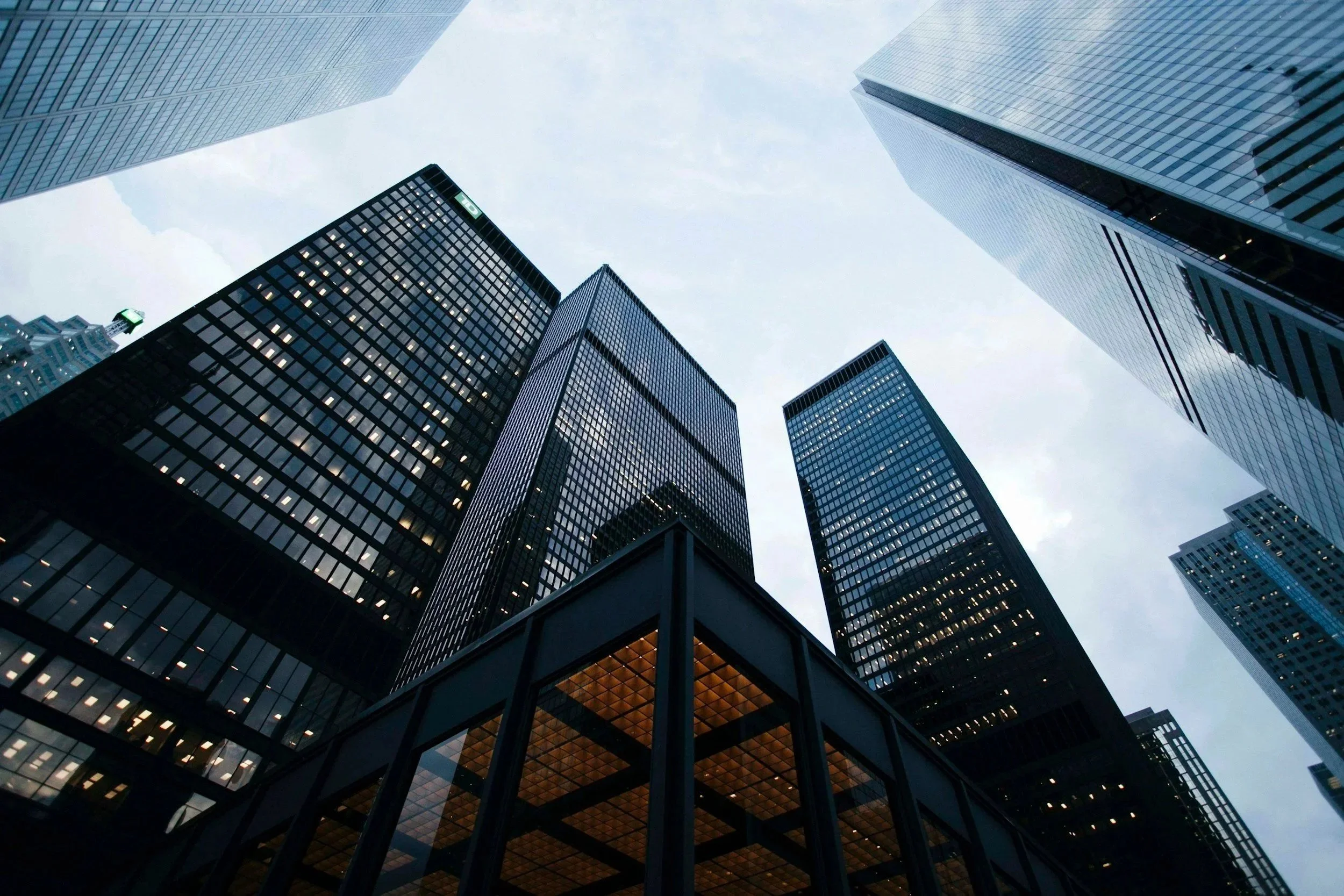 Looking up at tall glass skyscrapers in a city, with the sky visible through the buildings.