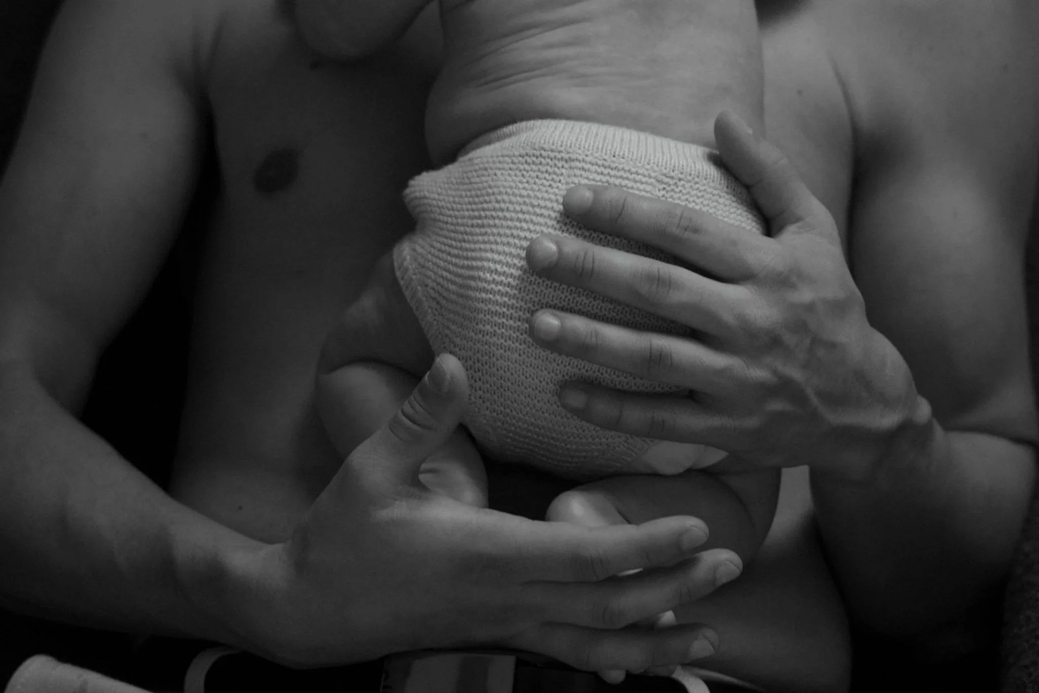 Une mère tenant un bébé contre sa poitrine, le bébé porte une couverture ou un vêtement en tricot. La photo est en noir et blanc.