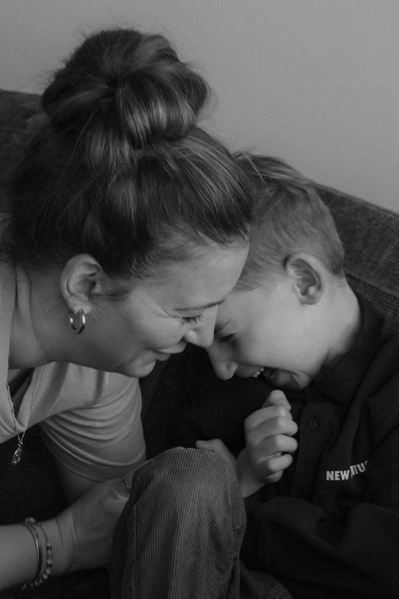 Une femme et un jeune garçon partagent un moment de tendresse, leur front et leur tête se touchant, en noir et blanc.