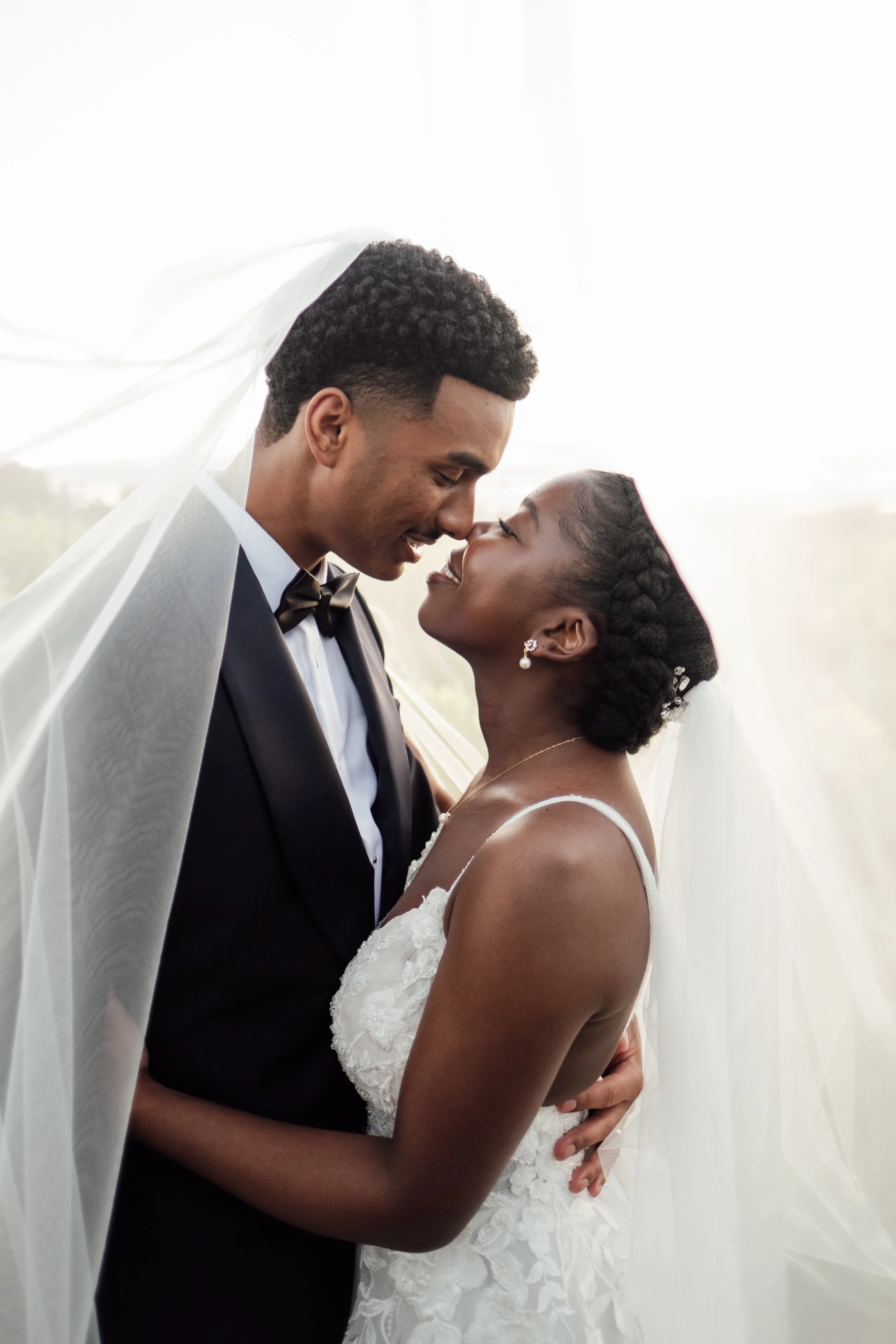 A bride and groom sharing a tender moment, with their foreheads touching and eyes closed, under the bride's veil during their wedding.