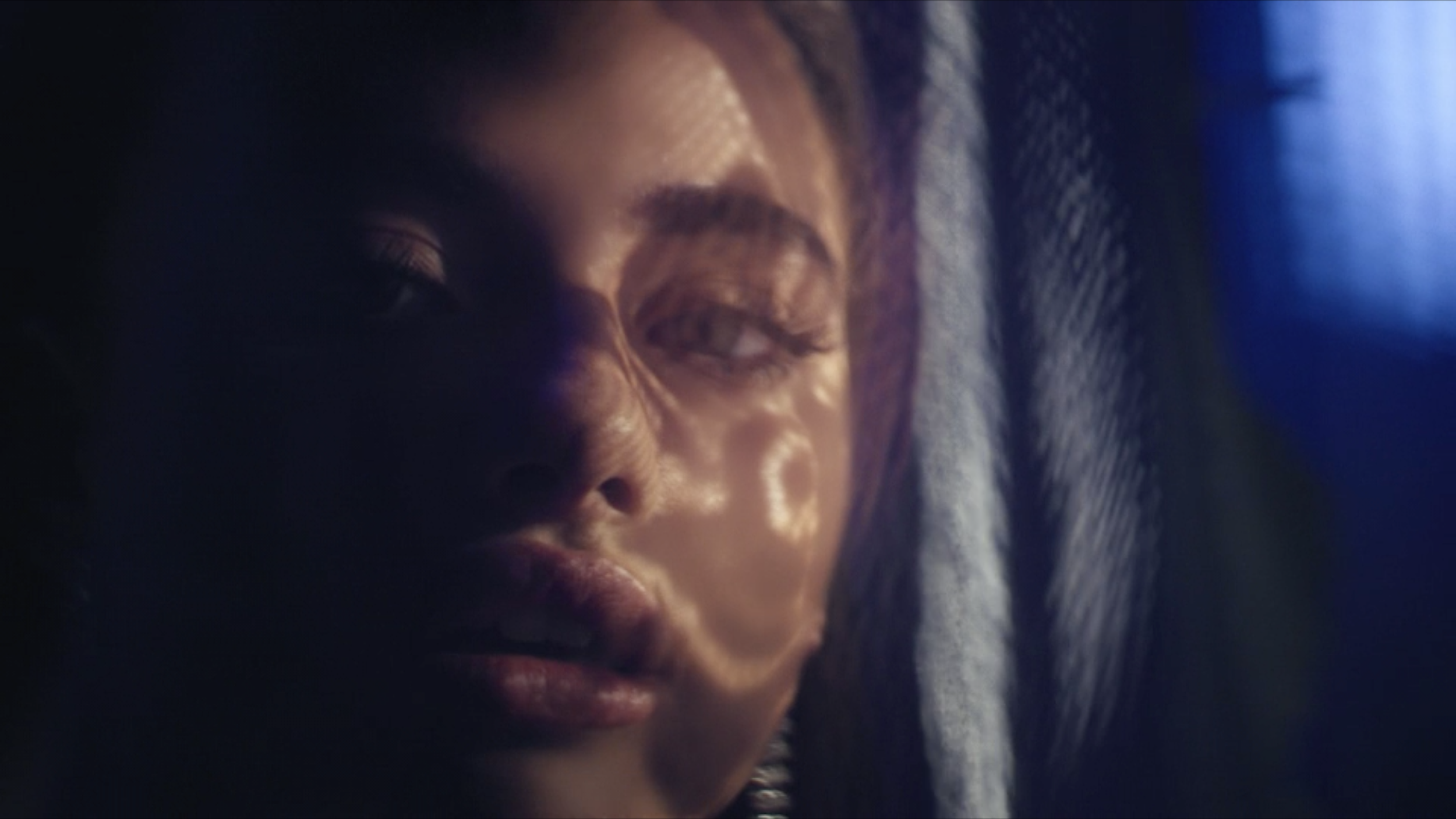 Close-up of a woman's face with dark hair, eyes closed, and a serene expression, lit with soft, moody lighting.