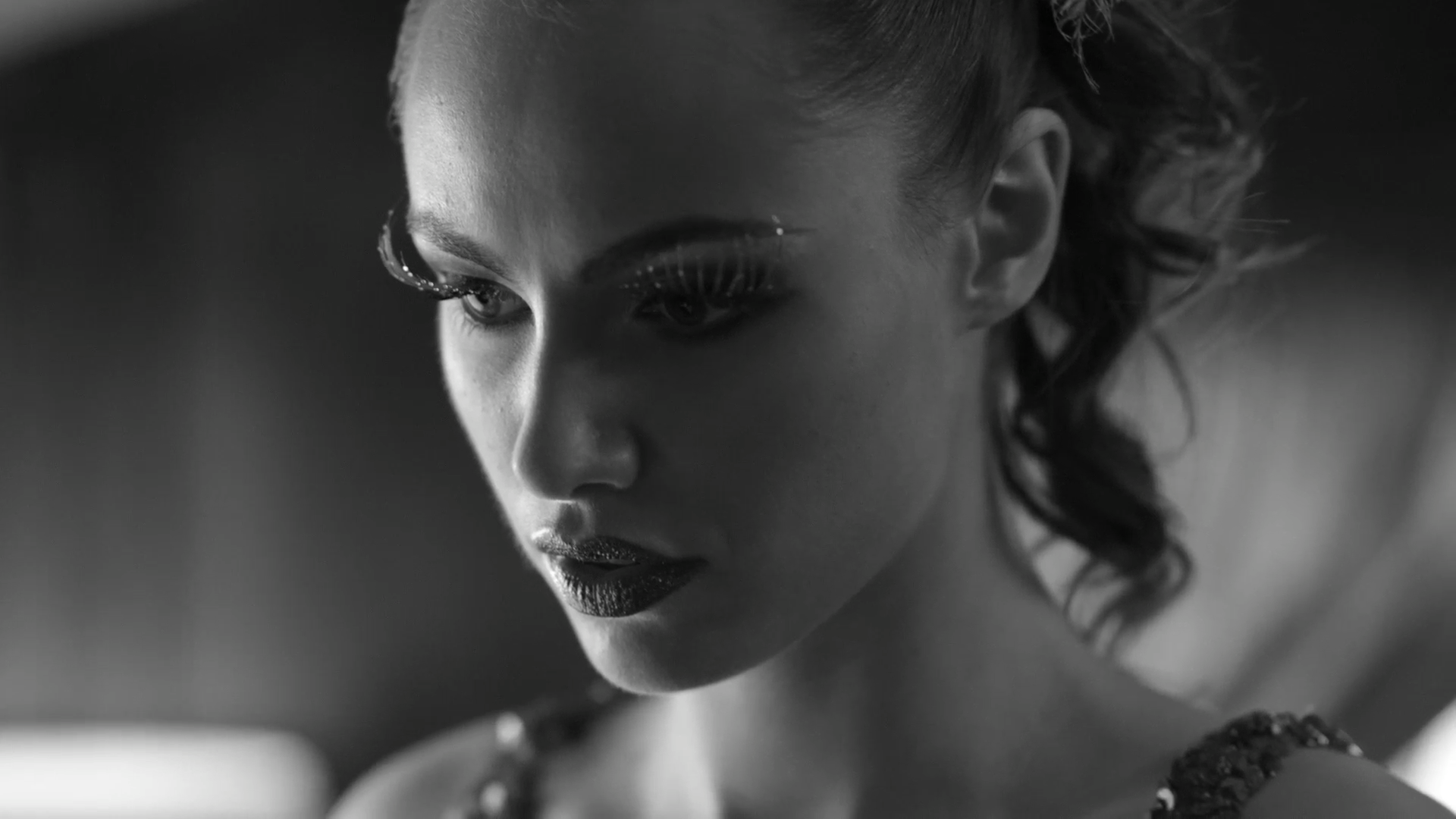 Close-up of a woman with glamorous makeup, curly hair, and a serious expression in black and white.