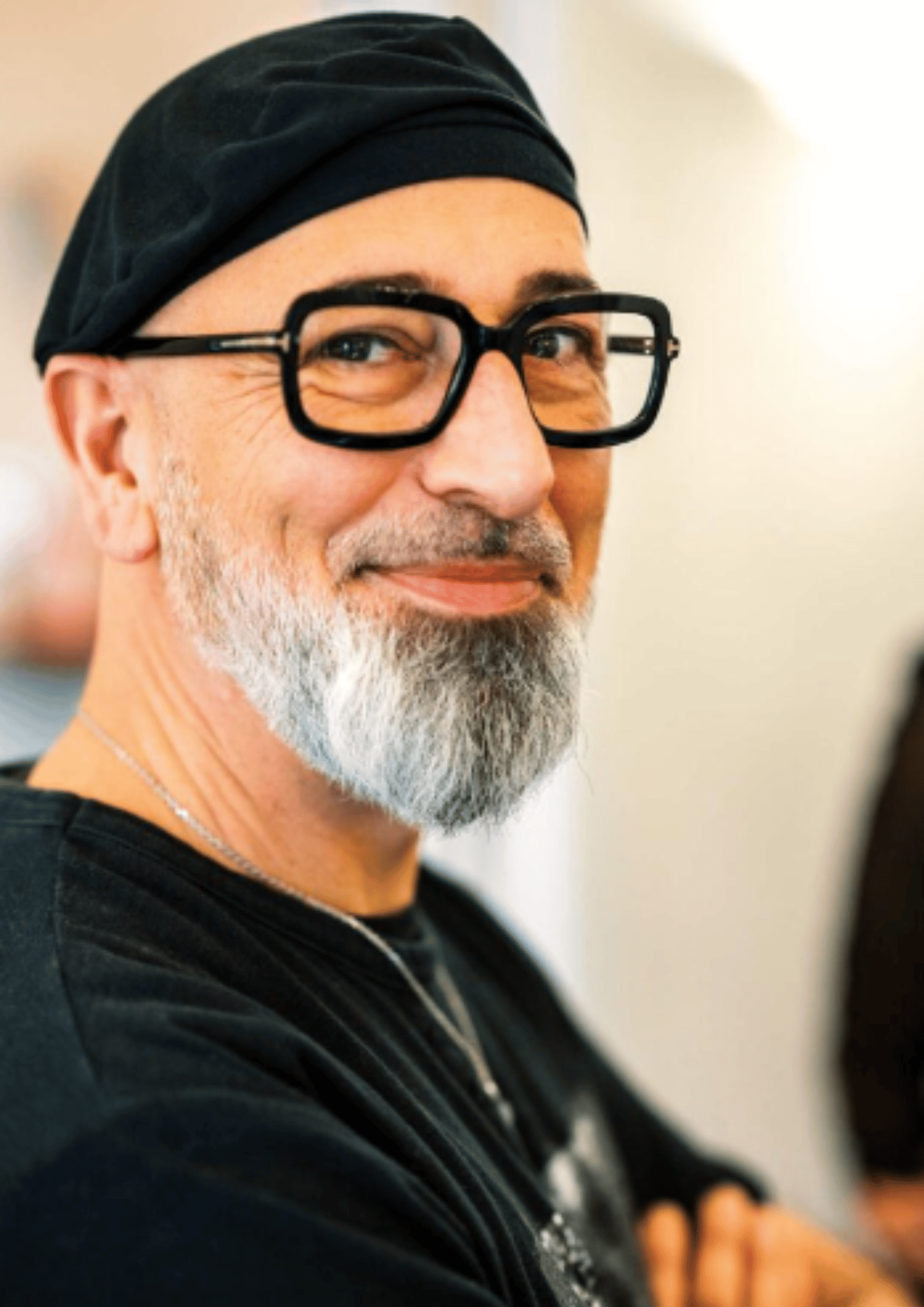 A middle-aged man with a beard and glasses wearing a black headscarf and a black shirt, smiling and looking to the side.
