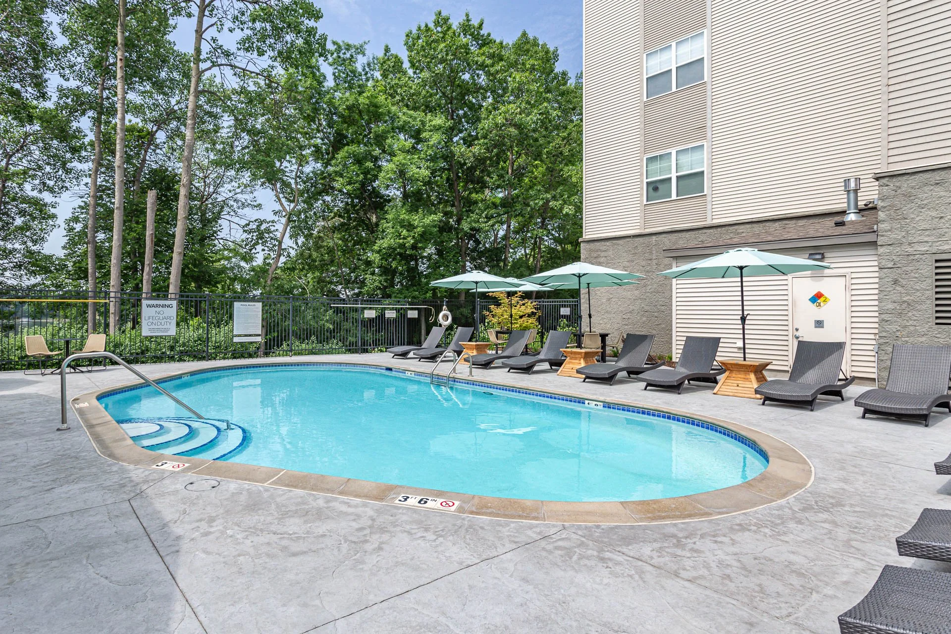 An outdoor swimming pool area with lounge chairs, umbrellas, and trees in the background.